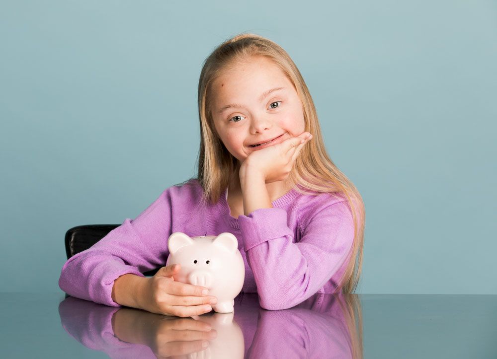 Mädchen mit Down-Syndrom und einem Sparschwein in der Hand