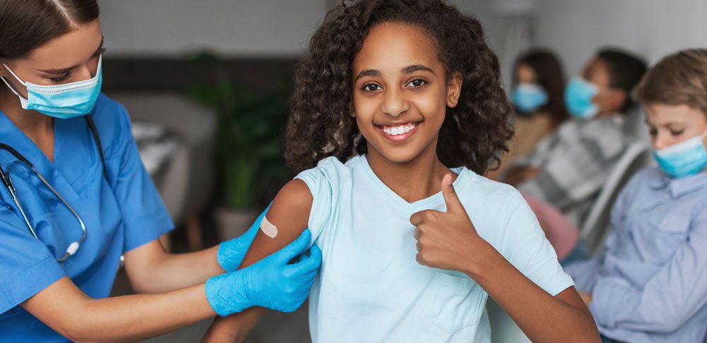Mädchen zeigt Daumen hoch und bekommt Pflaster von Krankenschwester auf den Arm